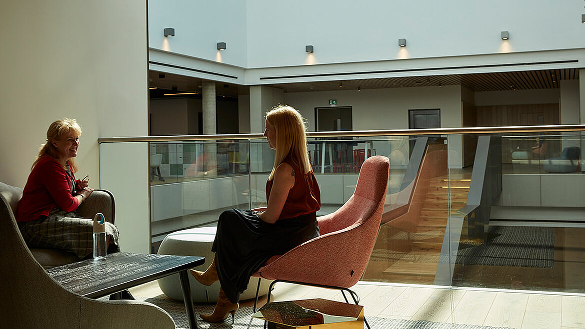 Zwei Frauen unterhalten sich in einer modern gestalteten, lichtdurchfluteten Lounge