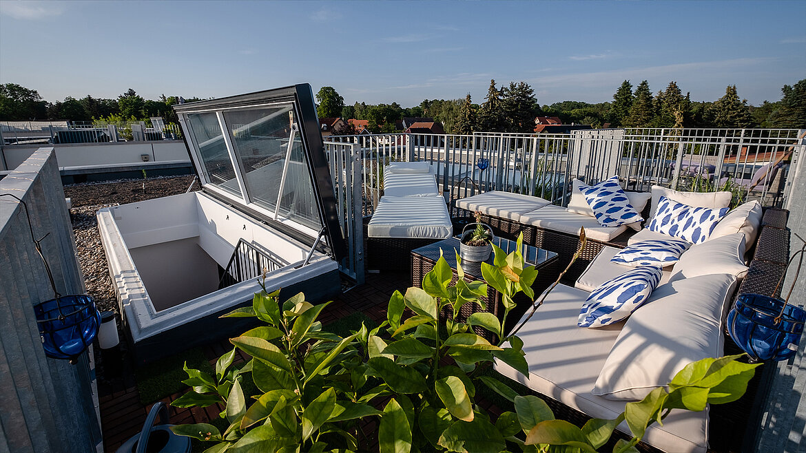 Moderne Dachterrasse mit Lounge-Möbeln, Pflanzen und einem offenen Glasdach-Zugang.