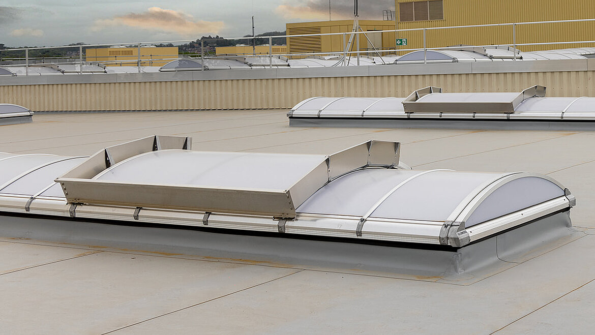 Neues LAMILUX Lichtband B nach Sanierung bei Heidelberger Druckmaschinen. Glänzende Fenster verbessern Belüftung und Energieeffizienz. Gelbes Industriegebäude im Hintergrund.