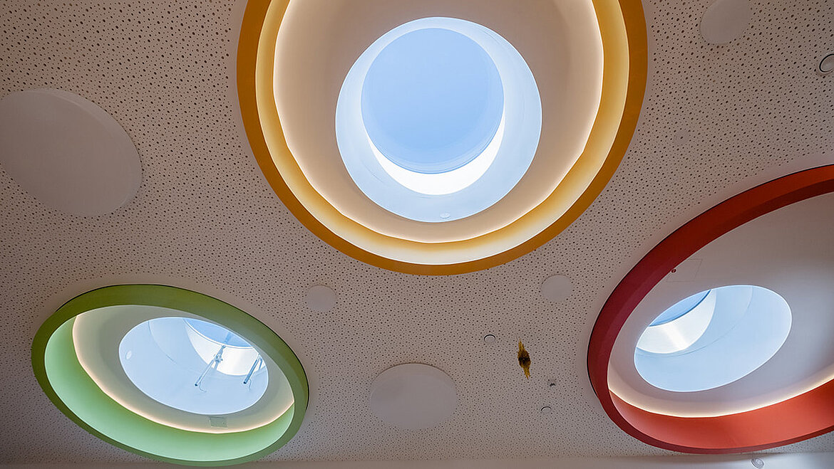 Okrągłe, szklane świetliki z kolorowymi akcentami w przedszkolu Sömmerda Projekt wnętrz z kolorowymi okrągłymi oknami do płaskich dachów w pokoju dziecinnym