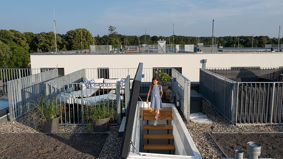 A girl in a blue dress climbs a staircase to the roof access of a modern terrace.