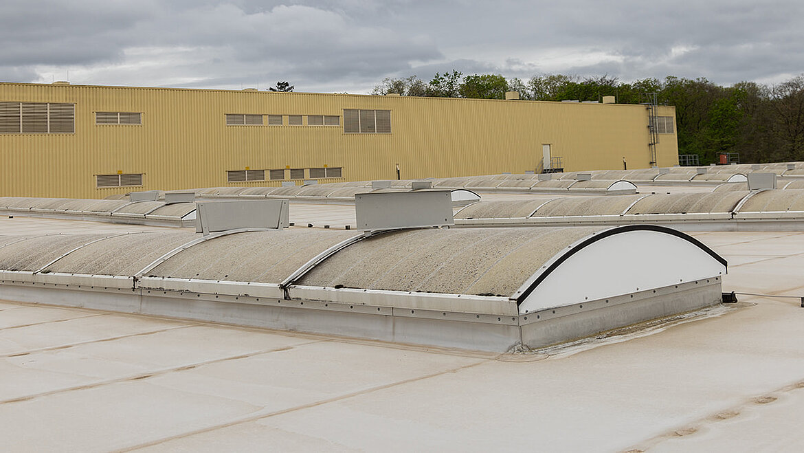 Veraltetes Lichttband vor Sanierung bei Heidelberger Druckmaschinen. Verschmutzte Fenster zeigen Abnutzung. Gelbes Industriegebäude im Hintergrund