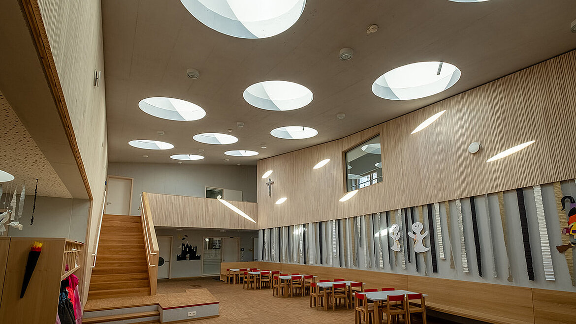 Wielofunkcyjna sala przedszkola St. Severin w Garching z okrągłymi oknami do płaskich dachów Gra światła z okrągłych, szklanych świetlików w salonie przedszkola