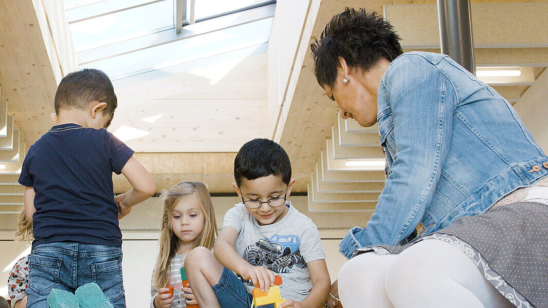 Dzieci bawią się pod szklanym dachem w swoim przedszkolu System światła dziennego firmy LAMILUX w pokoju dziecięcym nad placem zabaw